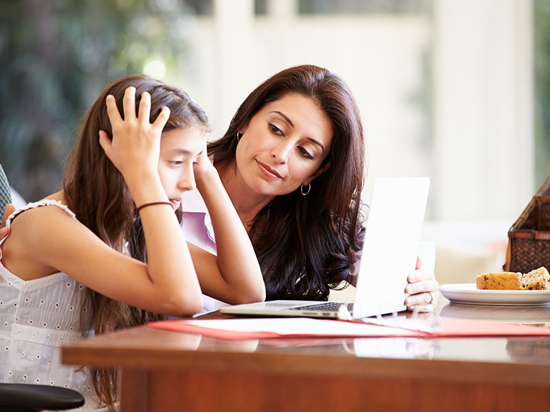 Mother,Helping,Stressed,Teenage,Daughter,Looking,At,Laptop