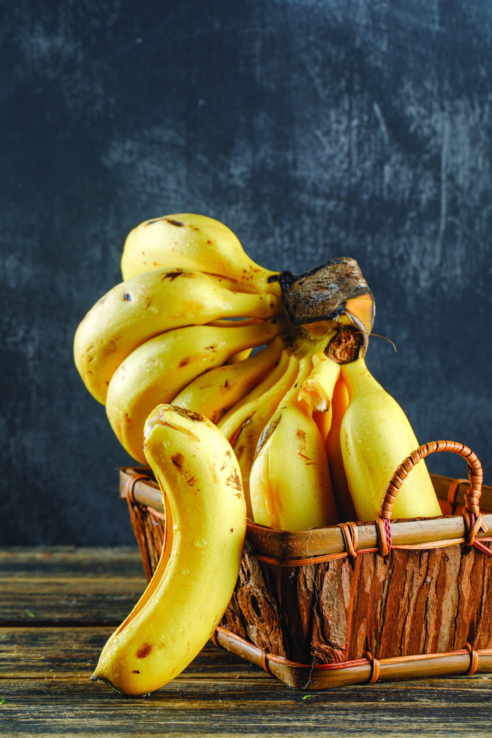 Bananas in a basket on wooden and plaster background. side view.