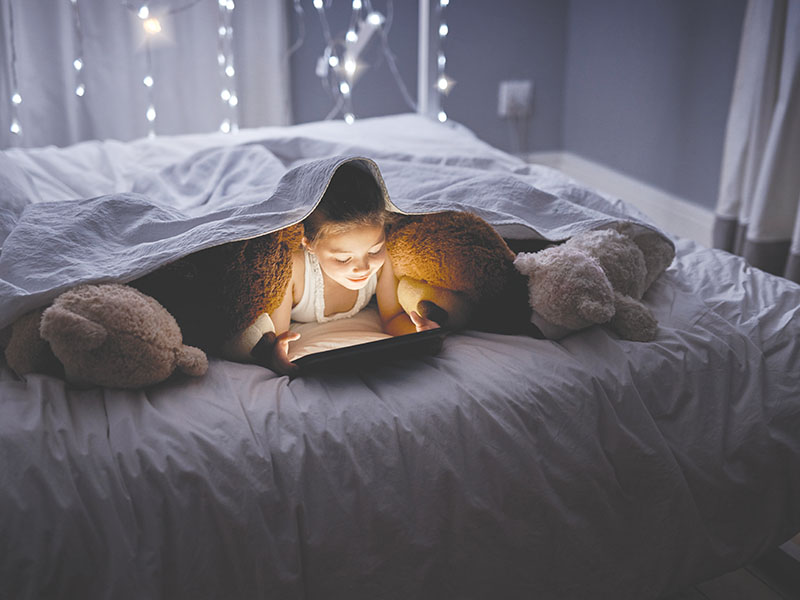 Tablet, reading and kid at night with video, story and youth game with fantasy and language learning app. Tech, teddy bear and young girl with scroll, relax and evening at home in bed on internet